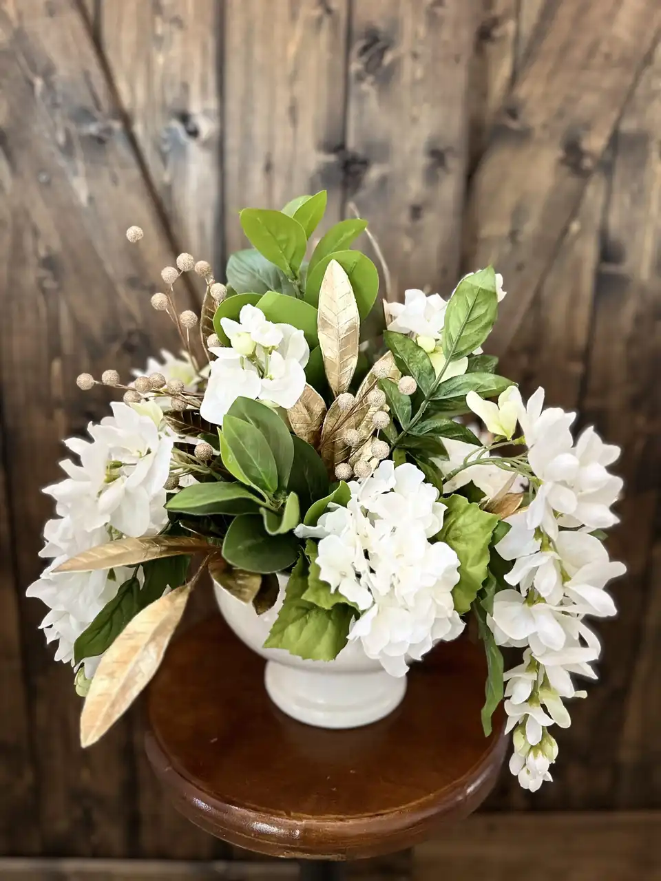 All-white arrangement of hydrangea, orchids and greenery in a white pedestal pot