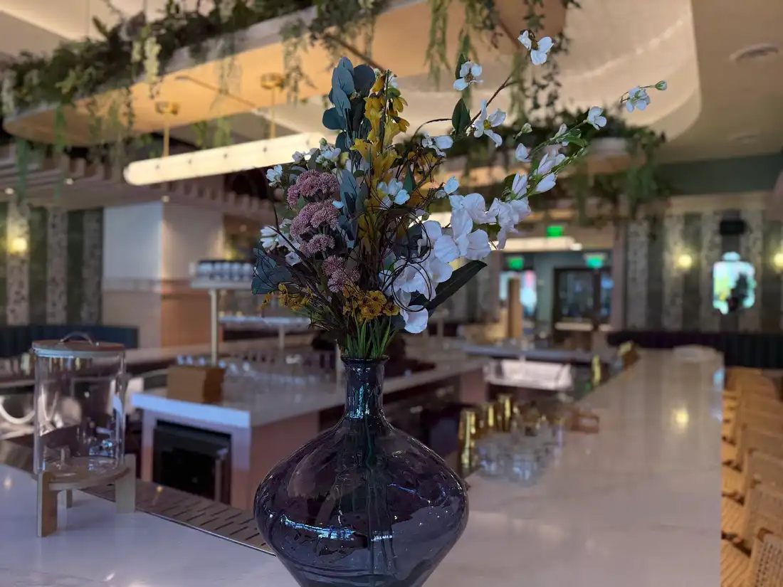 Smoked glass vase of white dogwood, pink sedum and yellow blooms on a marble restaurant bar