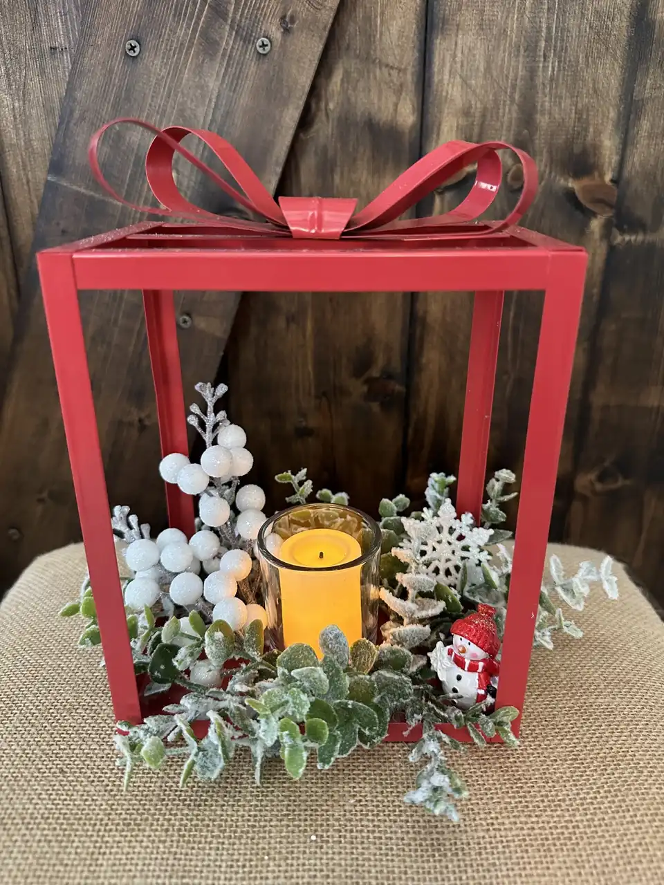 Red metal gift box frame filled with white berries, pine and a candle