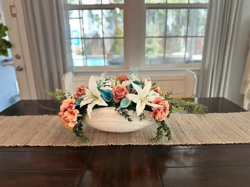 Long coastal-inspired dining centerpiece of lilies and coral roses on a farmhouse table