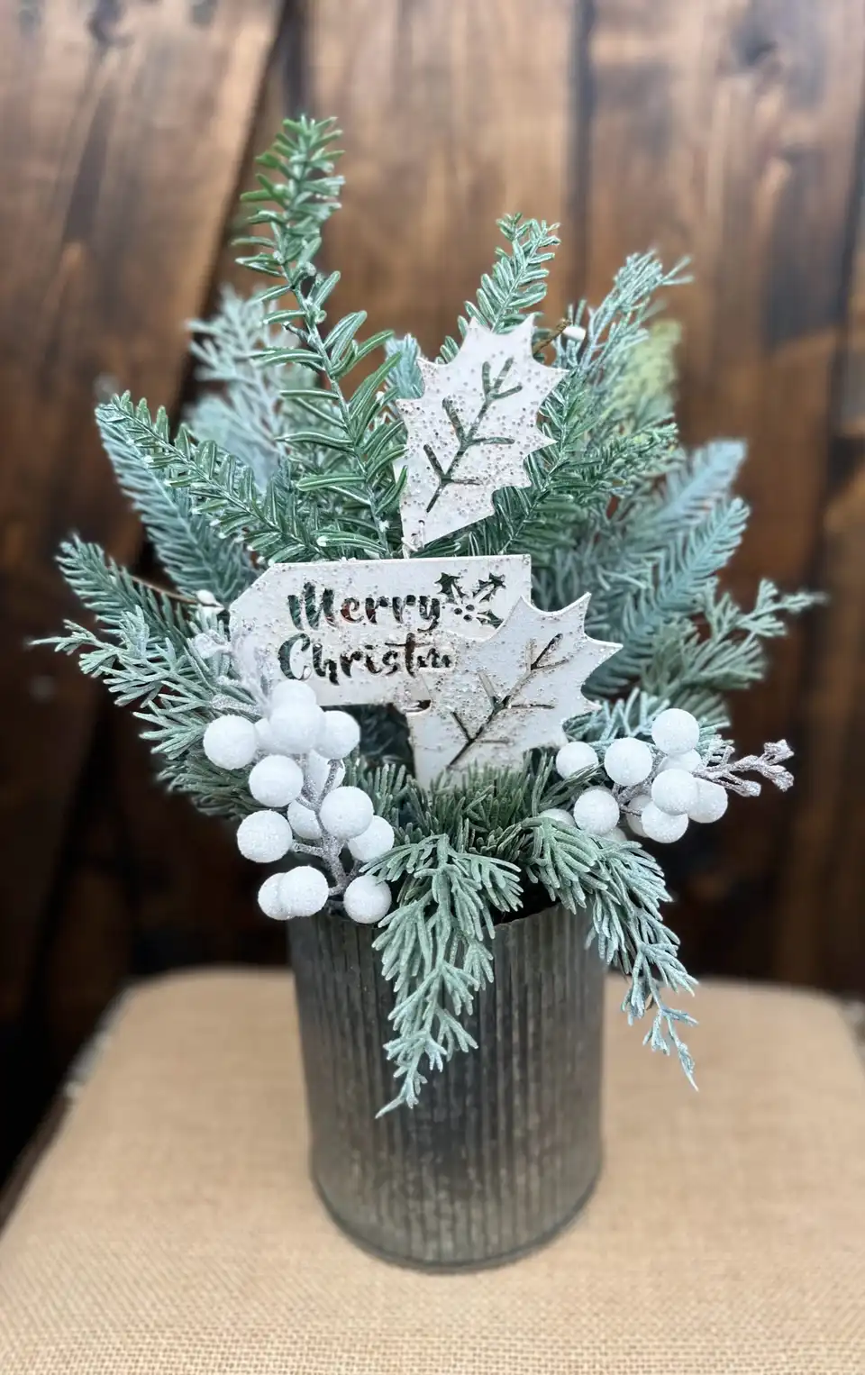 Frosted winter greenery with white berries and a Merry Christmas sign in a galvanized pail