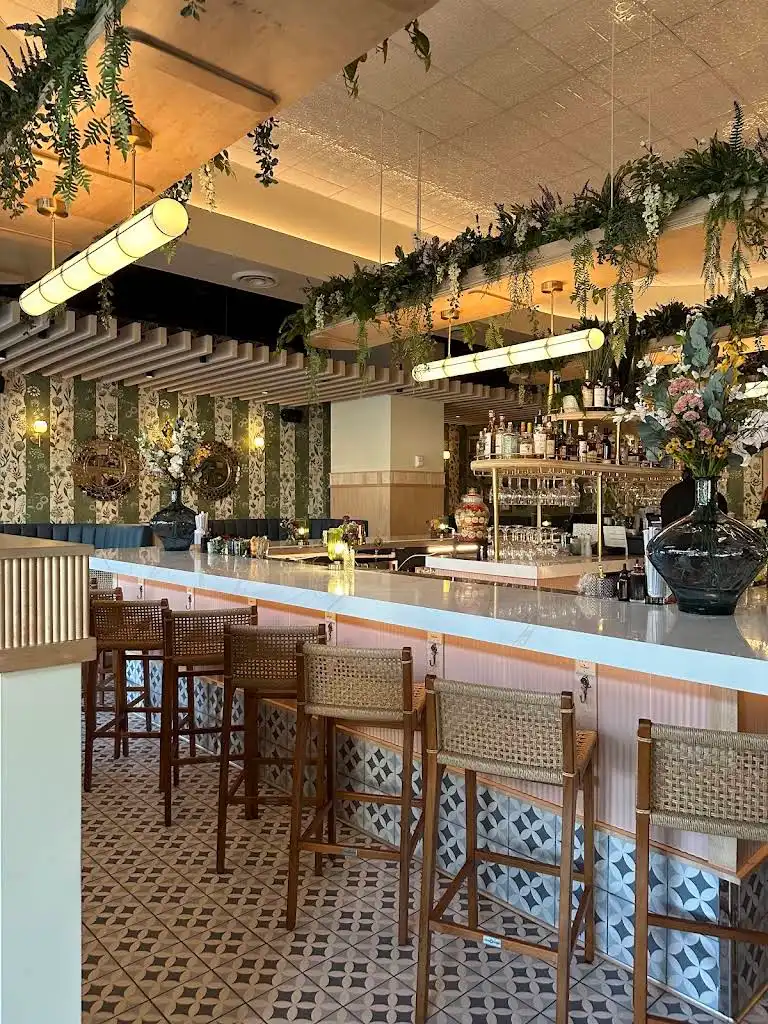 Hanging faux greenery and wisteria installation above a restaurant bar with tall floral vases