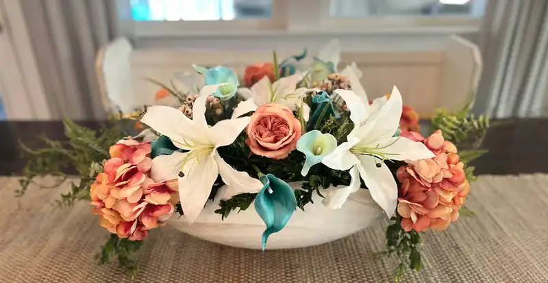 Low dining centerpiece of white lilies, coral roses and teal calla lilies in a white bowl