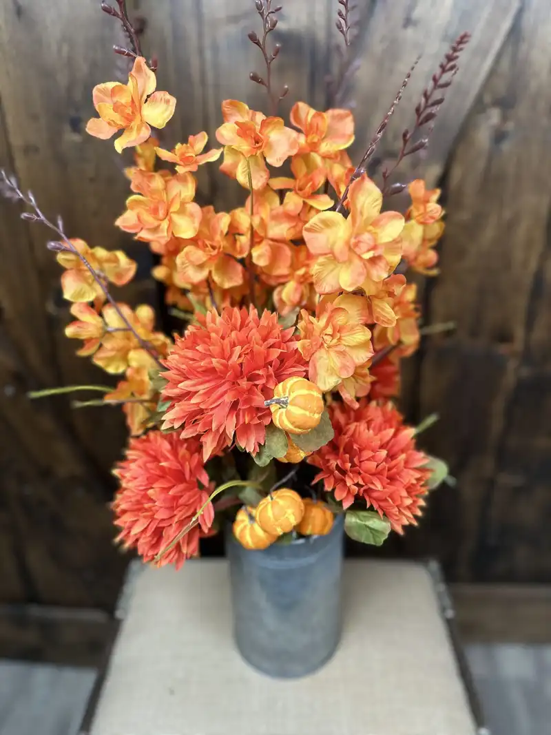 Bright orange orchids, dahlias and mini pumpkins in a tin vase