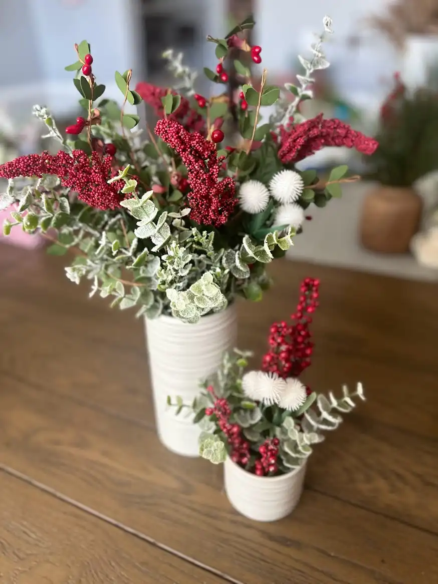 Pair of red berry and eucalyptus holiday arrangements in white vases