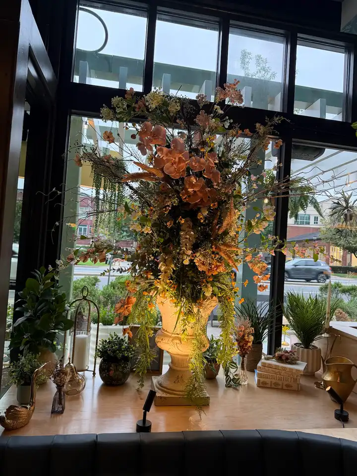 Lit stone urn overflowing with blush orchids and wild branches in a restaurant window at dusk